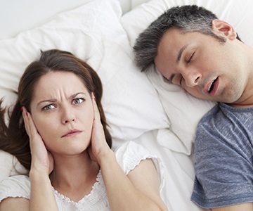 Woman covering ears next to snoring man