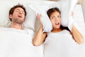 a man snoring and a woman using a pillow to cover her ears