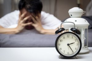 a man looking tired and an alarm clock reading early morning hours