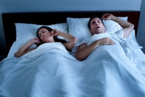 a man snoring and a woman plugging her ears while sleeping