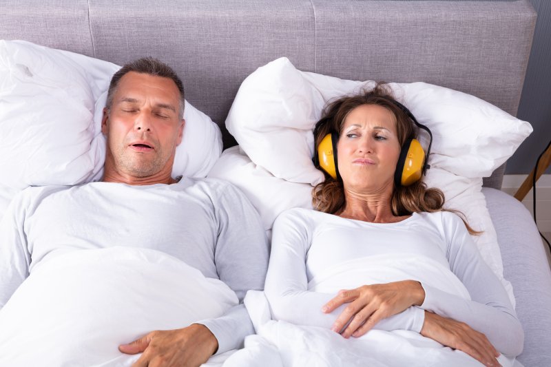 Man with sleep apnea snoring, woman wearing headphones