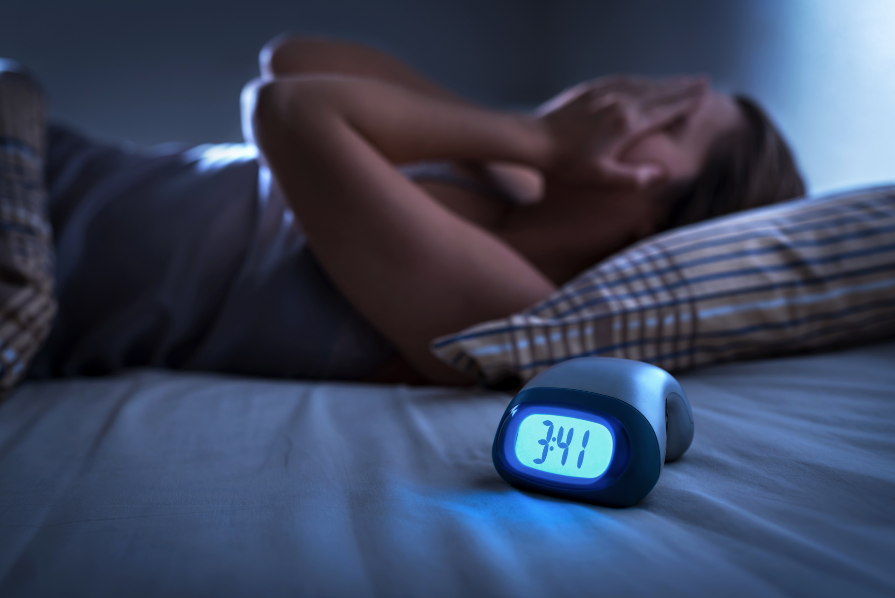 Woman trying to sleep, covering face with hands with alarm clock in the foreground
