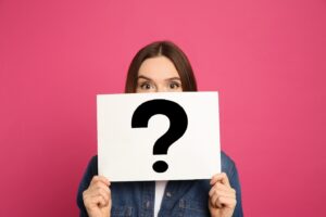 Woman holding sign up with a big question mark covering most of her face.